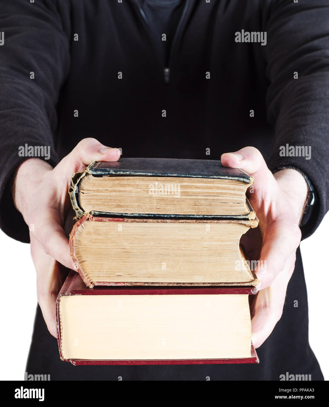 A pile of three old text books, handed forward to viewer by man in dark casual clothing. Stock Photo