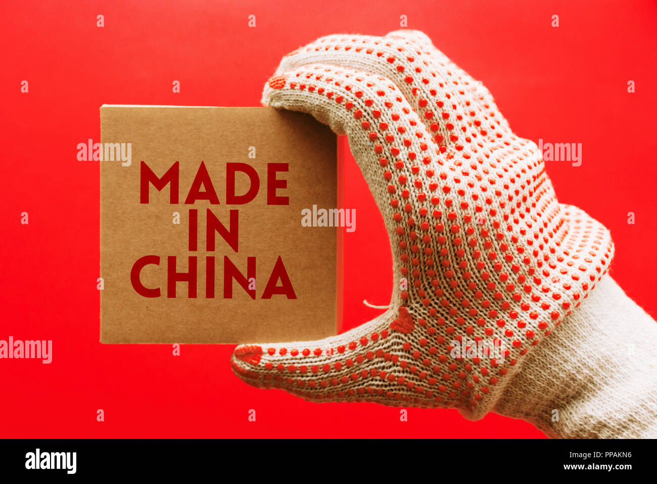 Made in China, worker with protective gloves holding cardboard product package over red background which is the primary color of Chinese national flag Stock Photo