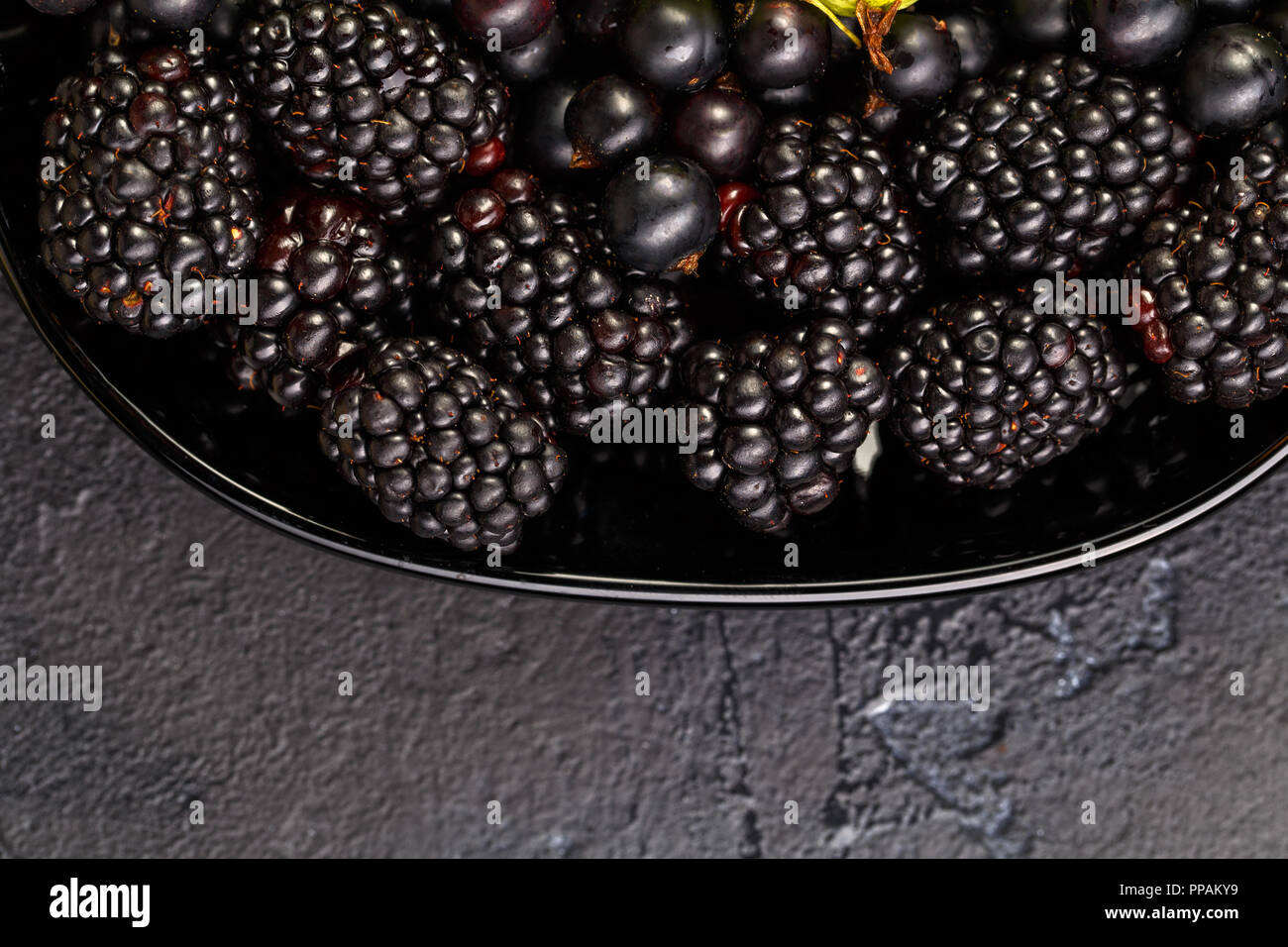 Photo on top of blackberries, black currant on black plate on black empty background Stock Photo