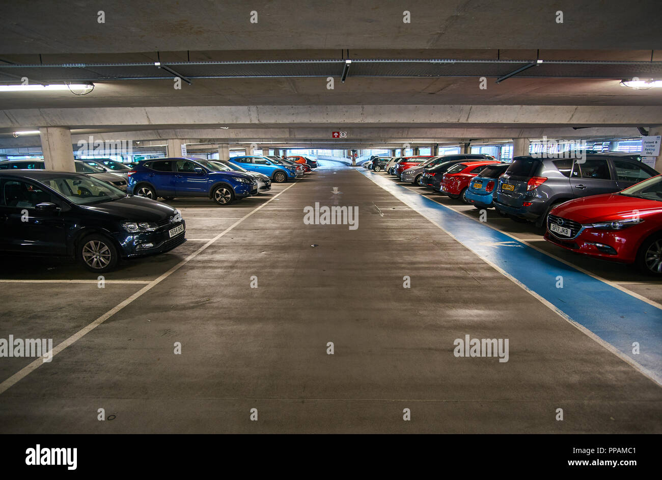 Underground multi storey car park / parking garage with cars parked on both sides. Stock Photo