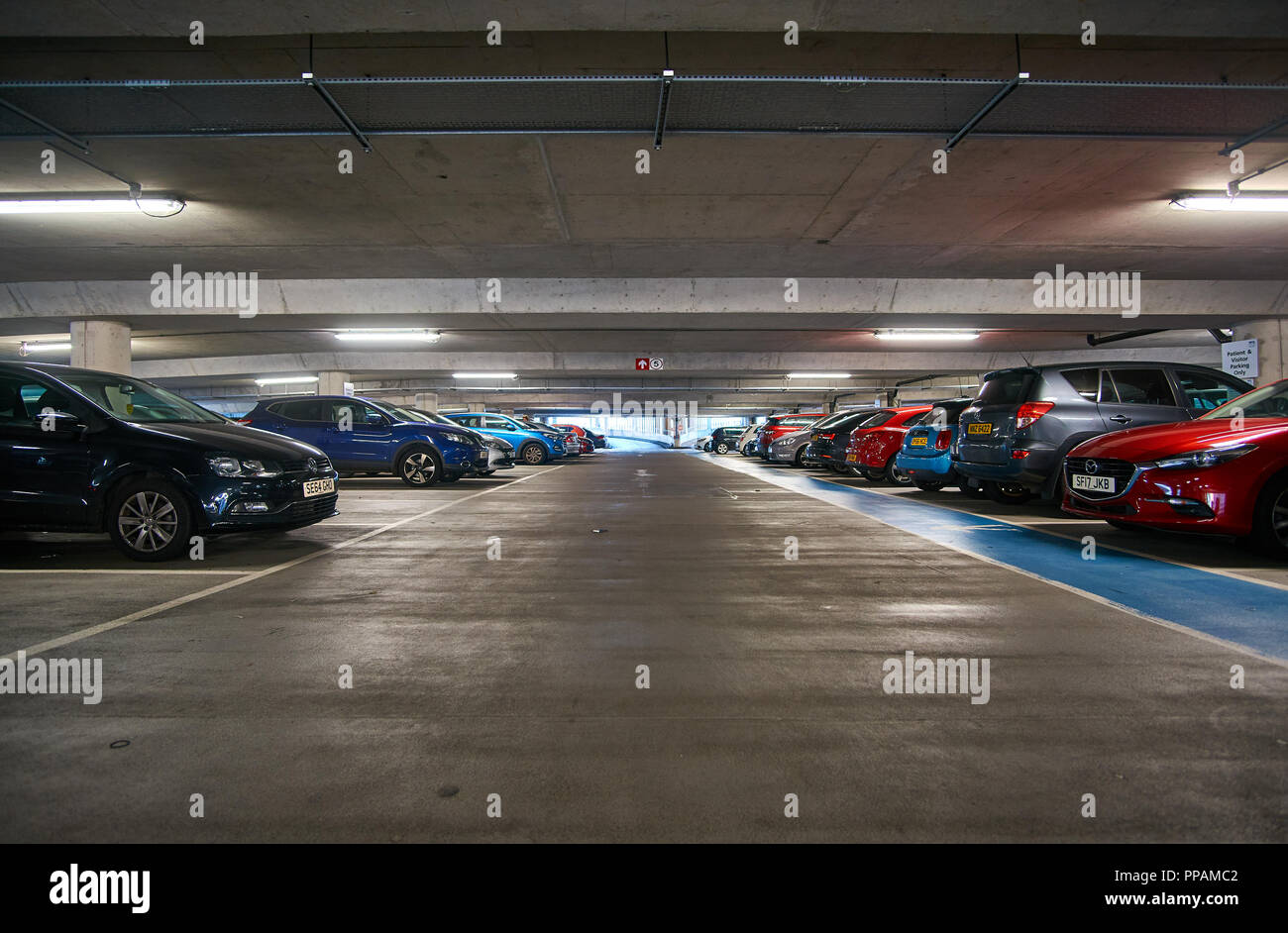 Underground multi storey car park / parking garage with cars parked on both sides. Stock Photo