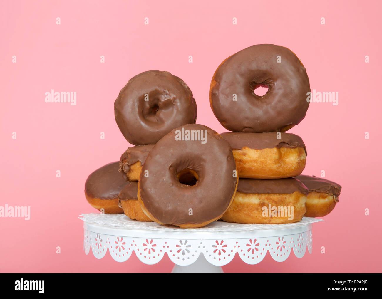 Many cake donuts frosted in chocolate stacked on a latticed white pedestal on a pink background with copy space Stock Photo