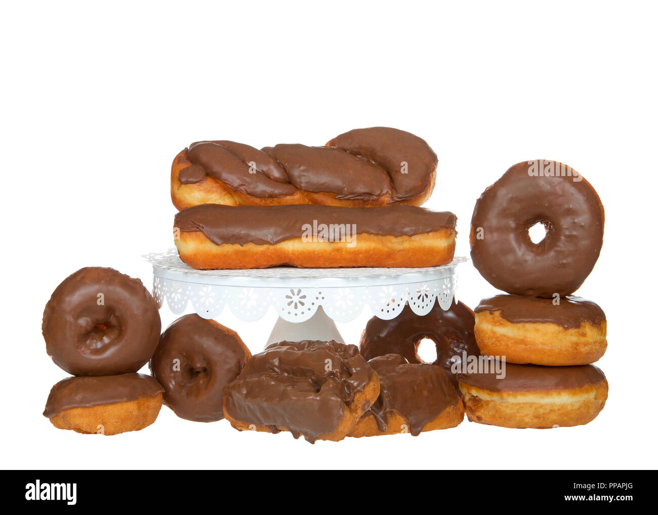 Many cake donuts, glazed twist, bar and old fashioned donuts frosted in chocolate isolated on white background with some on white pedestal. Stock Photo