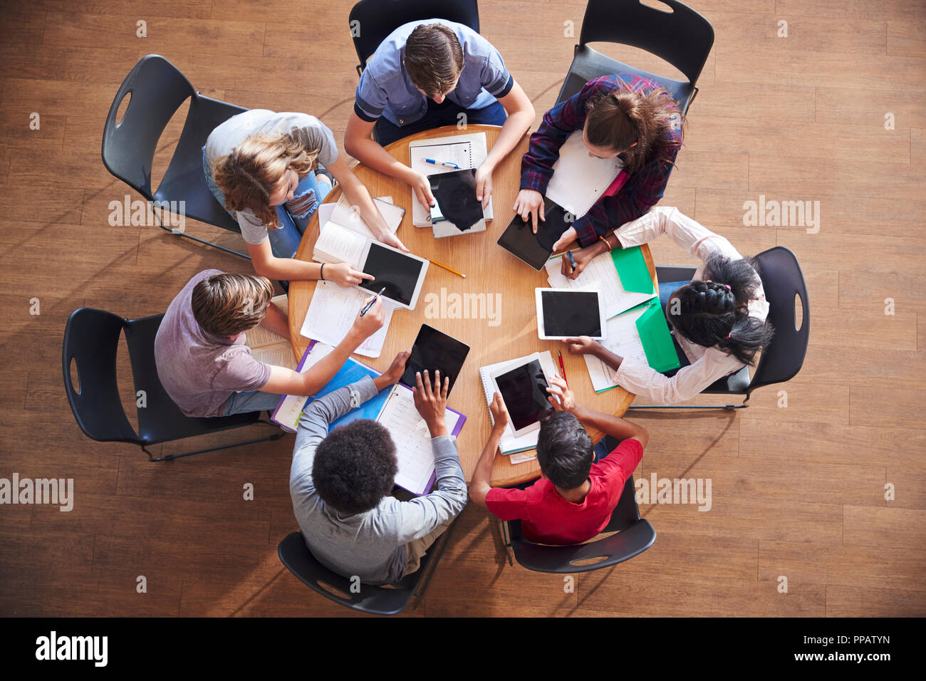 Overhead Shot Of High School Pupils Using Digital Tablets In Group Study Around Tables Stock Photo