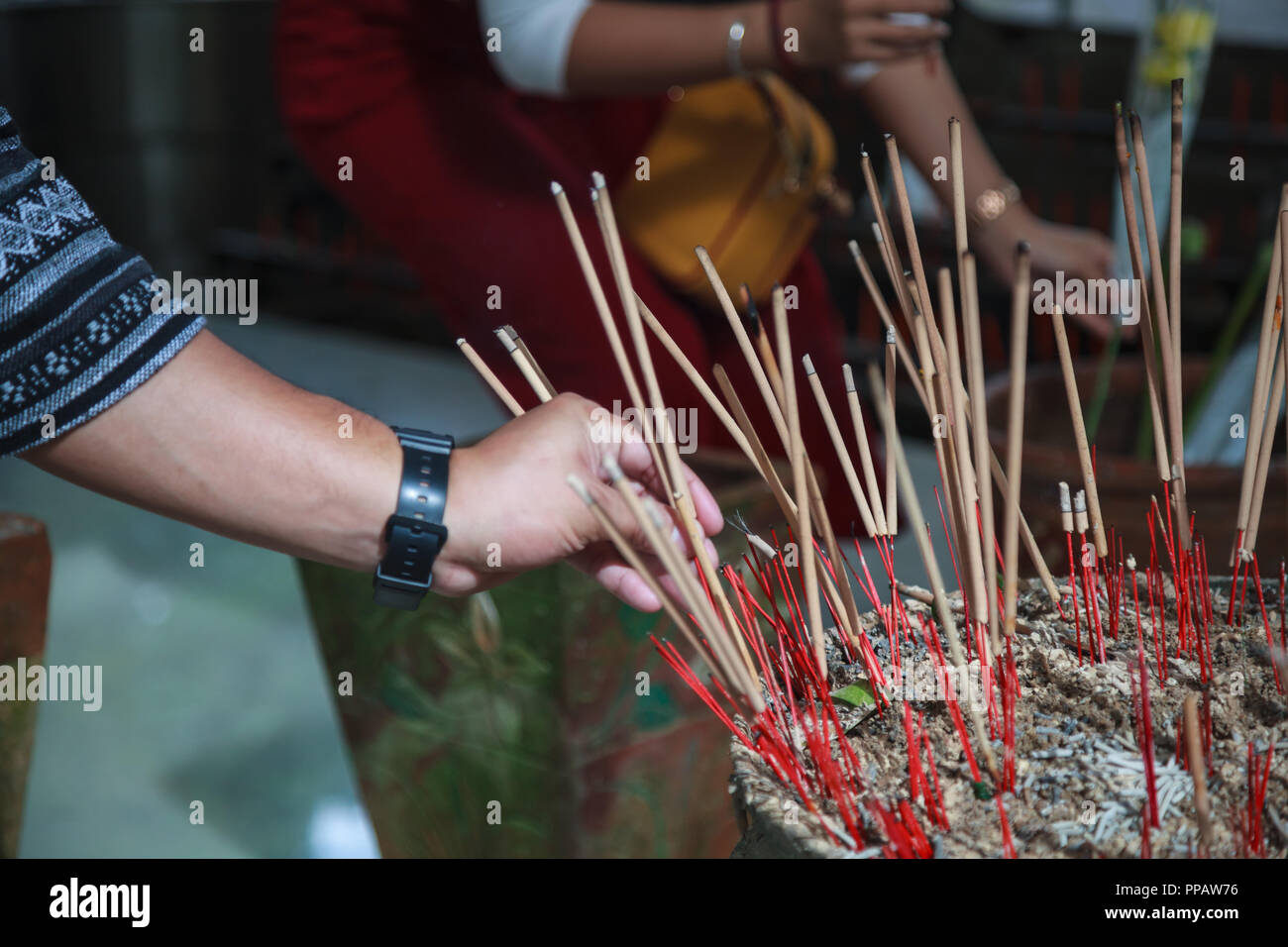 man hand sticks burning incense in incense pot in Buddhist Temple