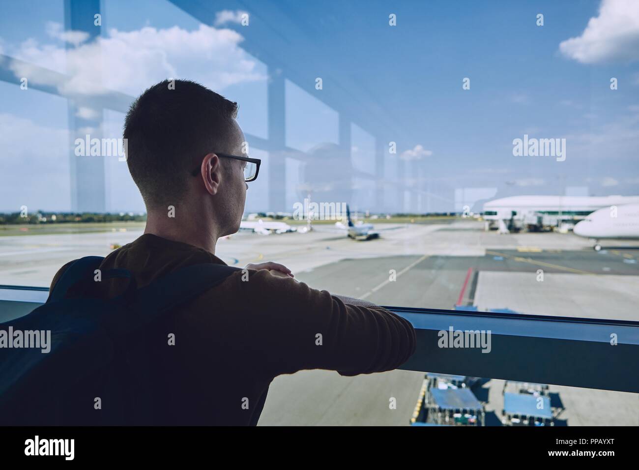 Young passenger waiting at airport and looking through window to airplane. Stock Photo
