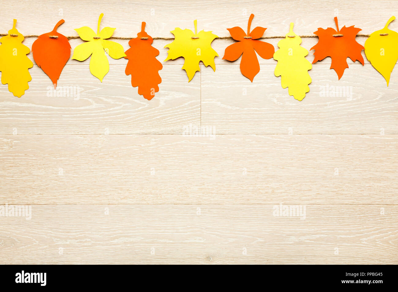 Simple, rustic country style Fall Thanksgiving decorations garland banner of colorful cut paper leaves on whitewashed wood background Stock Photo