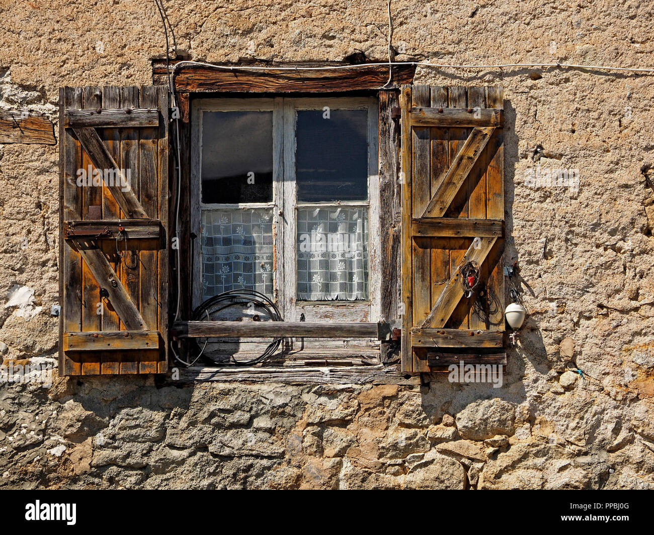 flaking paint on window with bare wooden shutters and coiled electrical