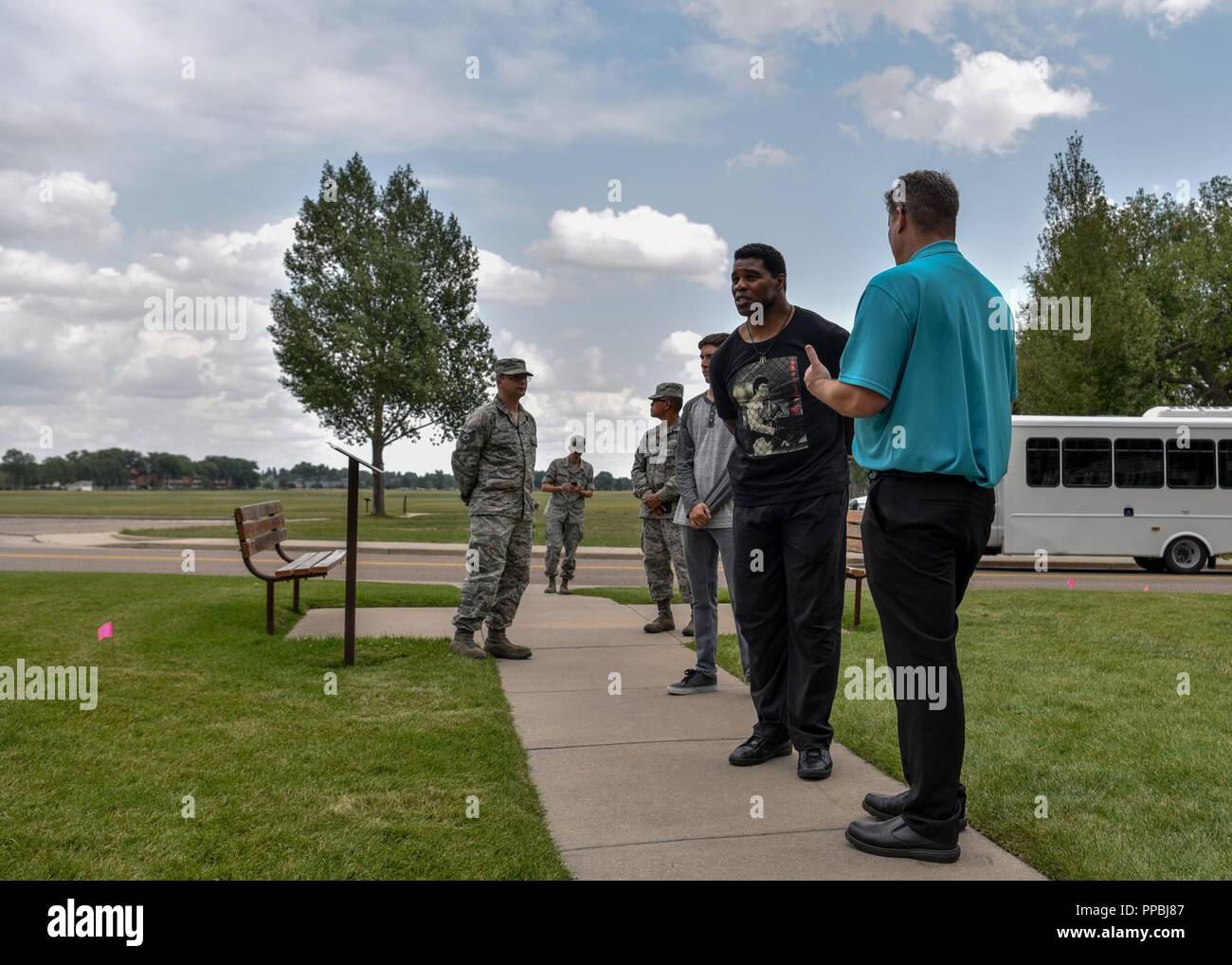 Herschel Walker, 1982 Heisman Trophy winner, listens to Glenn Robertson, 90th Missile Wing tour guide, during a tour of F.E. Warren Air Force Base, Wyo., Aug. 14, 2018. During the tour, Walker learned about the rich history of F.E. Warren AFB. Stock Photo