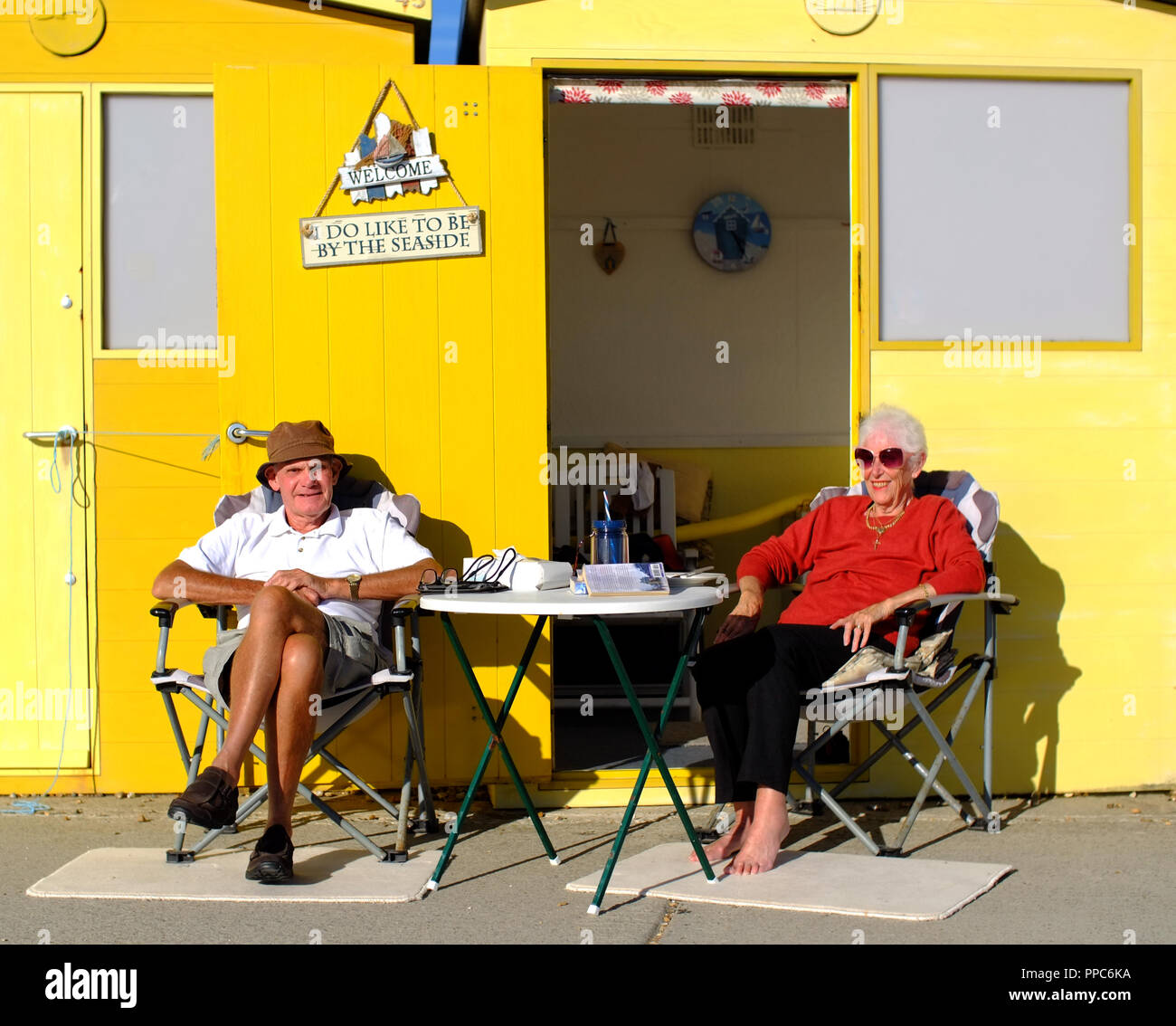 Couple enjoying the sun outside their beach hut in Seaford, East Sussex. Uk Stock Photo