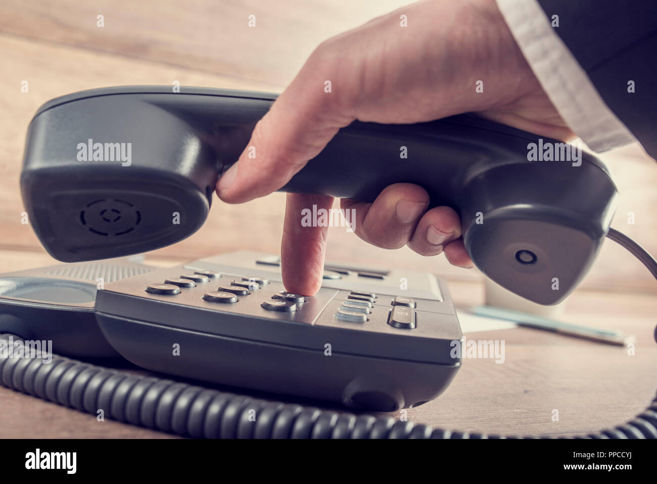 Closeup of businessman making a telephone call by dialing a phone number on a classical black landline device with a retro faded look. Stock Photo
