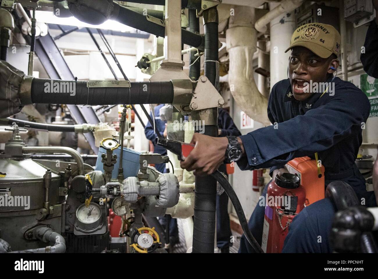 SEA (Aug. 31, 2018) Electrician’s Mate 3rd Class Levon King fights a simulated fire during a general quarters drill aboard the Arleigh Burke-class guided-missile destroyer USS Carney (DDG 64) Aug. 31, 2018. Carney, forward-deployed to Rota, Spain, is on its fifth patrol in the U.S. 6th Fleet area of operations in support of regional allies and partners as well as U.S. national security interests in Europe and Africa. Stock Photo