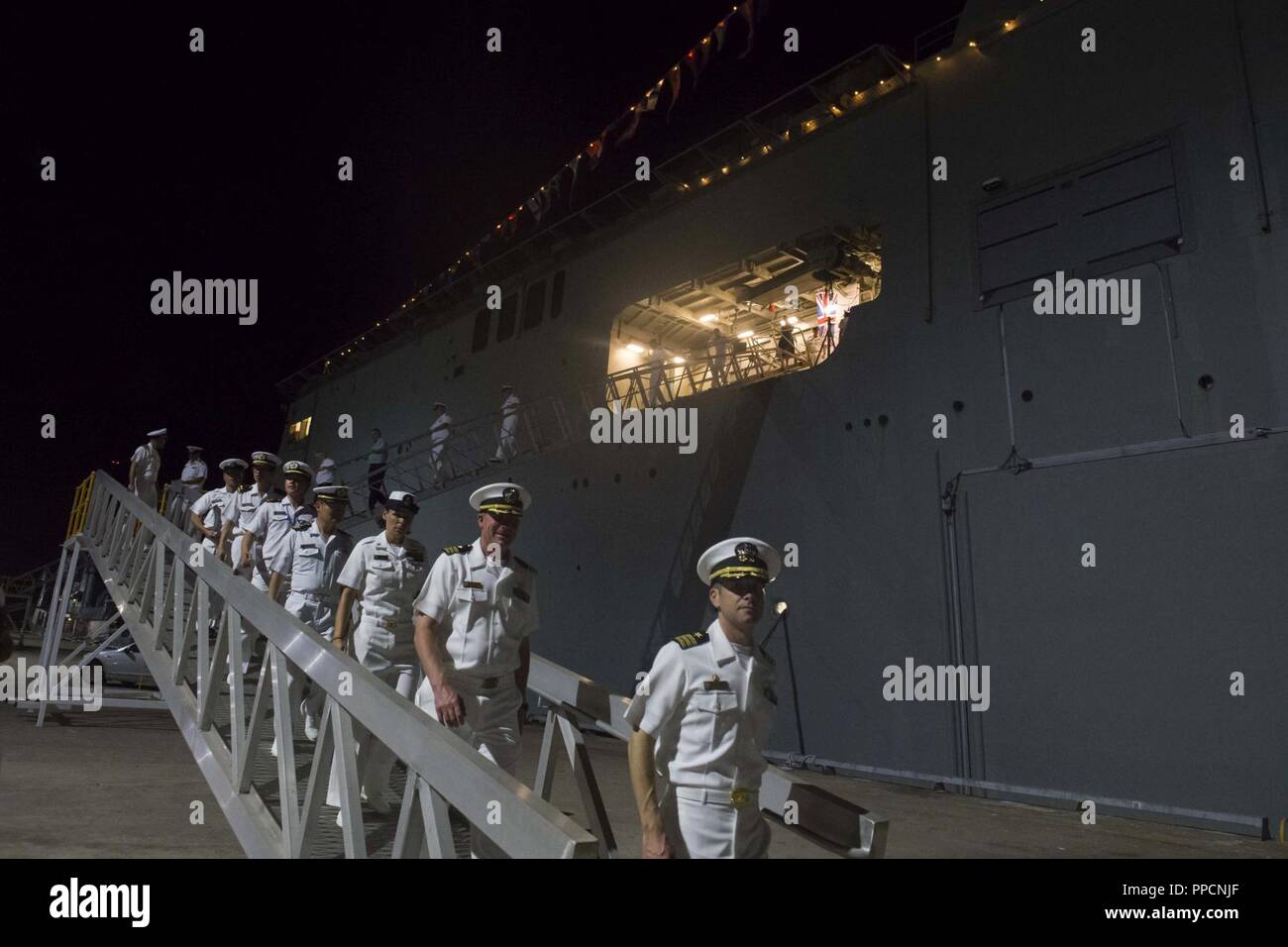 DARWIN, Australia (Aug. 31, 2018) Cmdr. Kevin Louis, front, commanding officer of the Arleigh-Burke class guided-missile destroyer USS Michael Murphy (DDG 112), and other guests depart Australian navy Canberra-class landing helicopter dock ship HMAS Canberra (L02) following the opening reception of Australian exercise Kakadu 2018. Michael Murphy is participating in Kakadu to enhance maritime security skills with participating nations by highlighting the value of information sharing and multilateral coordination. Stock Photo