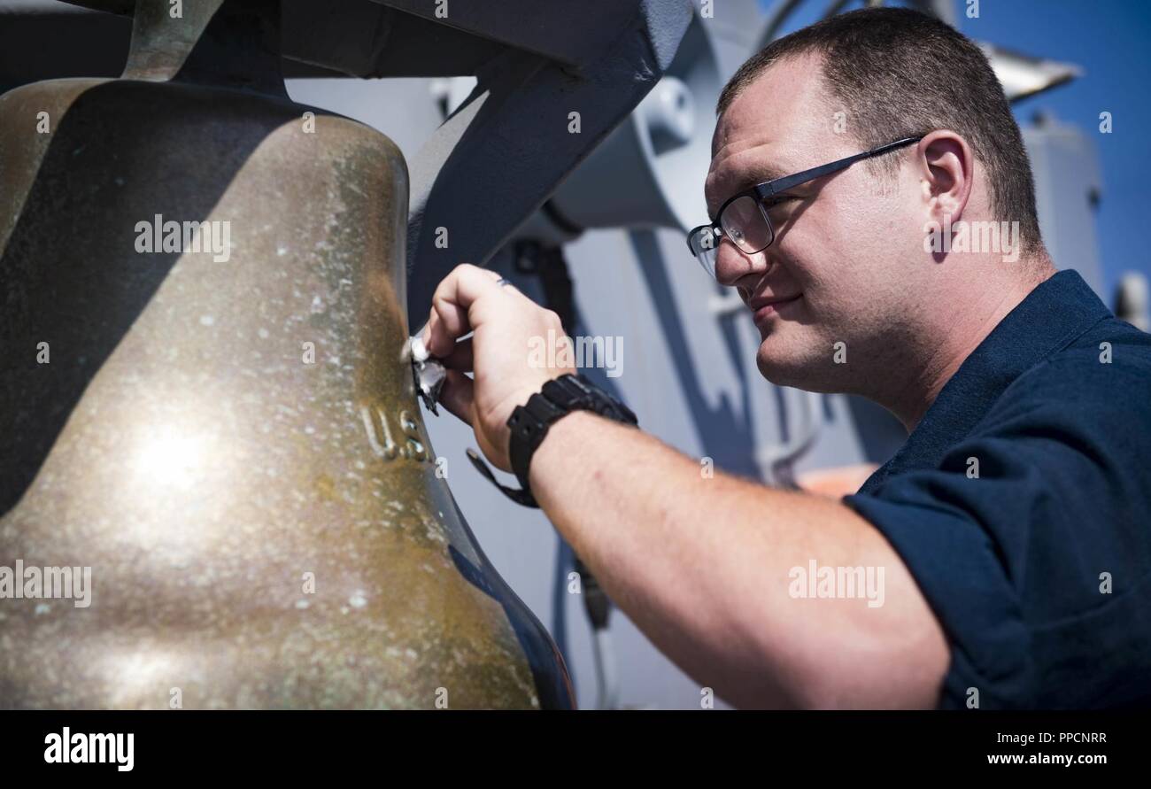 SEA (Sept. 4, 2018) Culinary Specialist 2nd Class Garrett Cook shines the ship’s bell aboard the Arleigh Burke-class guided-missile destroyer USS Carney (DDG 64) Sept. 4, 2018. Carney, forward-deployed to Rota, Spain, is on its fifth patrol in the U.S. 6th Fleet area of operations in support of regional allies and partners as well as U.S. national security interests in Europe and Africa. Stock Photo
