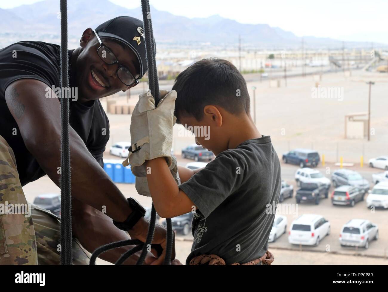 Sgt. Clint Sargent, 1st Armored Division Iron Training Detachment cadre, Fort Bliss, Texas, fastens a rope around a child’s Swiss seat on the rappel tower of the Air Assault Obstacle Course during the third annual Community Outreach Day at Fort Bliss Aug. 25. This year’s event was coordinated by the 210th RSG and the 1st Armored Division Iron Training Detachment - along with volunteers of Child Crisis Center, Big Brothers Big Sisters, and the El Paso Police Department – to mentor and interact with citizens of El Paso, Texas. Stock Photo