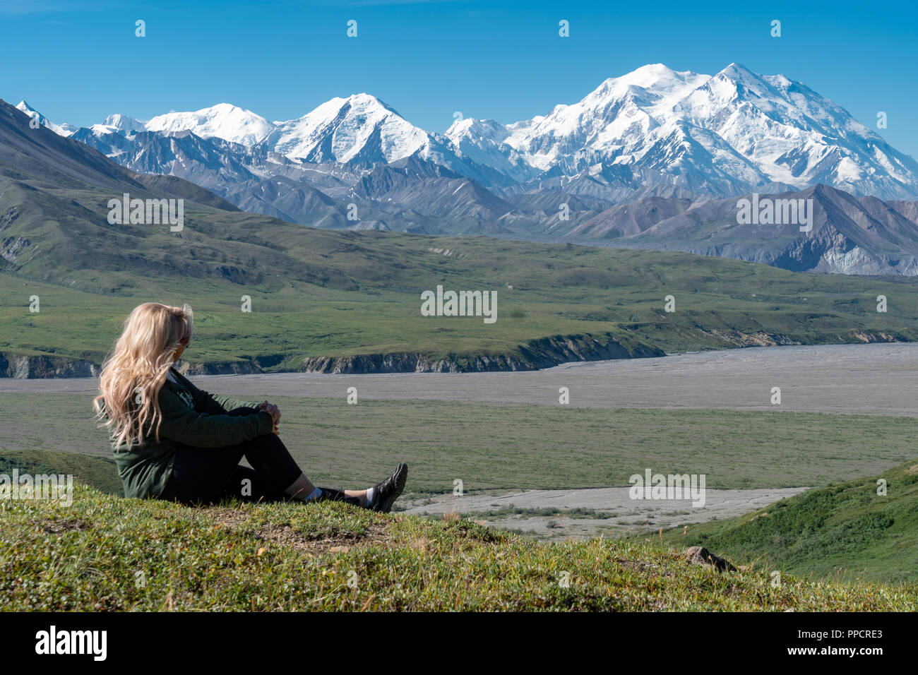 Adult female poses with a view of Denali (formerly Mt McKinley) in Denali National Park on a clear sunny day in the summer Stock Photo