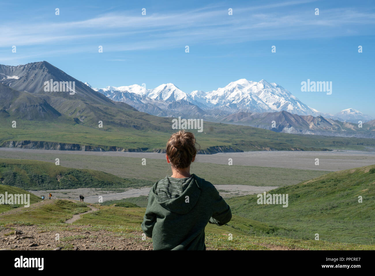 Adult female stands in front of Denali mountains in the Alaska Range of Denali National Park. Concept for solo female travel, confidence Stock Photo