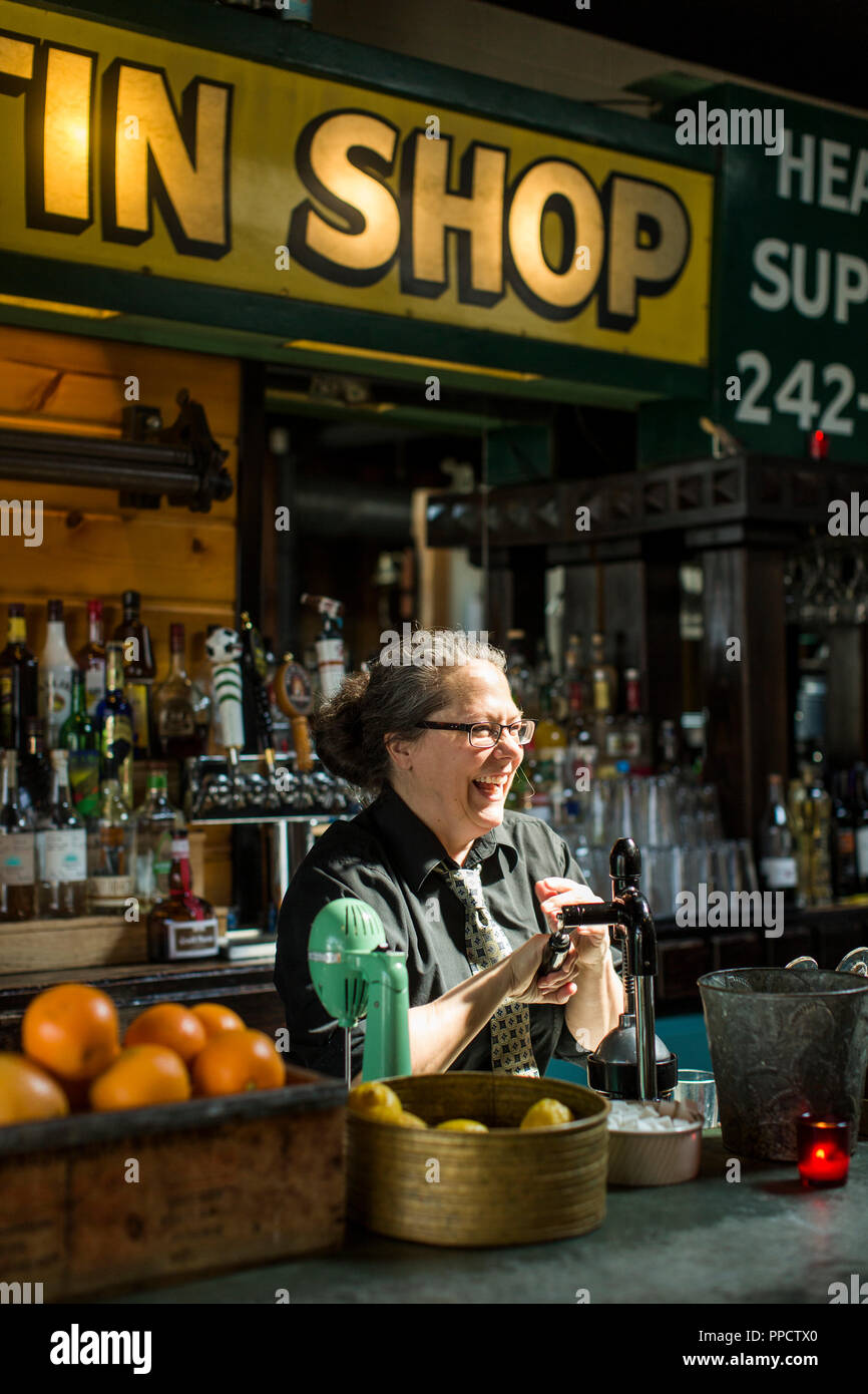 Female bartender laughing while preparing drink at bar, Seattle, Washington, USA Stock Photo