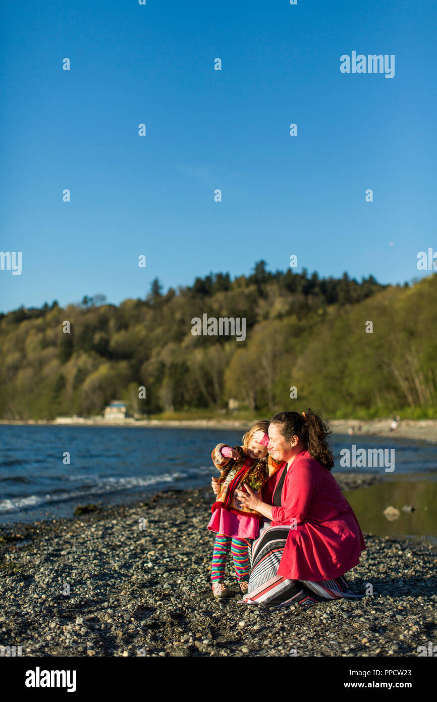 Mother and little daughter relaxing on rocky coastal beach, Seattle, Washington, USA Stock Photo