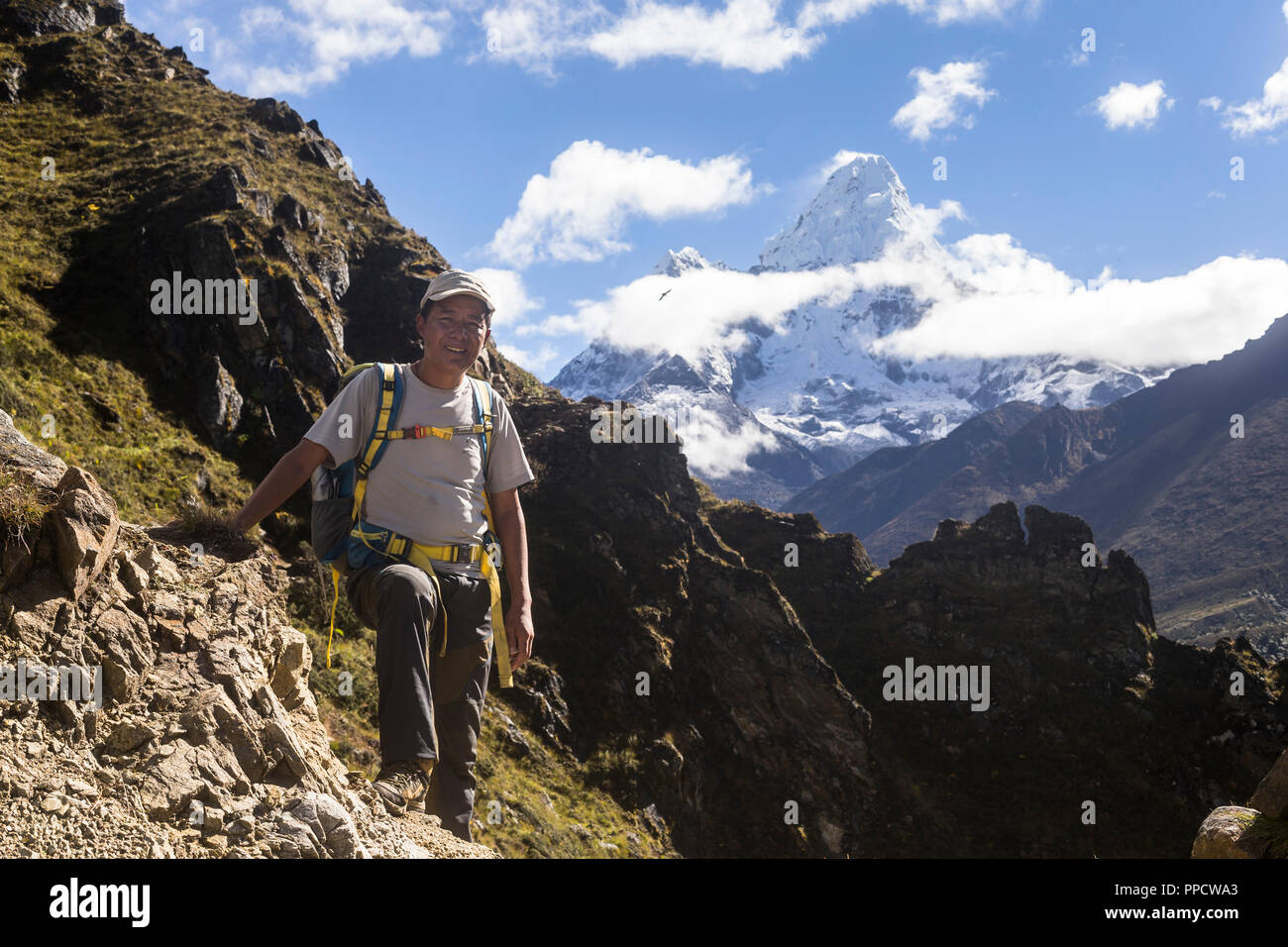 Sange Sherpa, a Nepalese mountain guide stands for a photo along the trekking route towards Everest Base Camp, Ama Dablam can be seen in the distance, which the guide has climbed before, Phortse, Solu Khumbu, Nepal Stock Photo