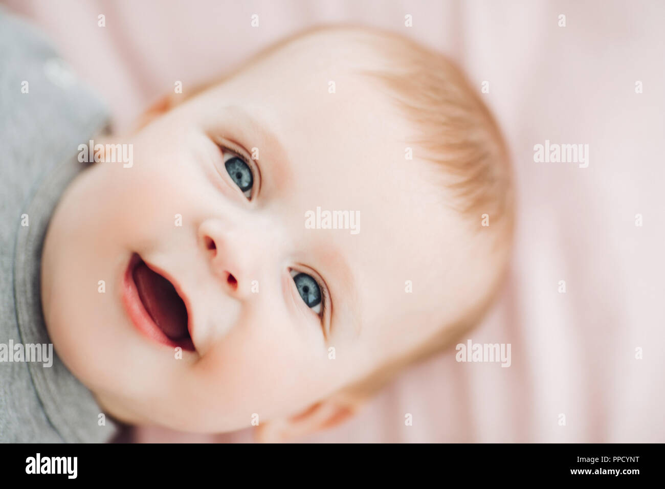 Close up of cute baby boy with big blue eyes, wearing in grey clothes, lying on bed and looking at camera. Kid resting, playing. Concept of child and  Stock Photo