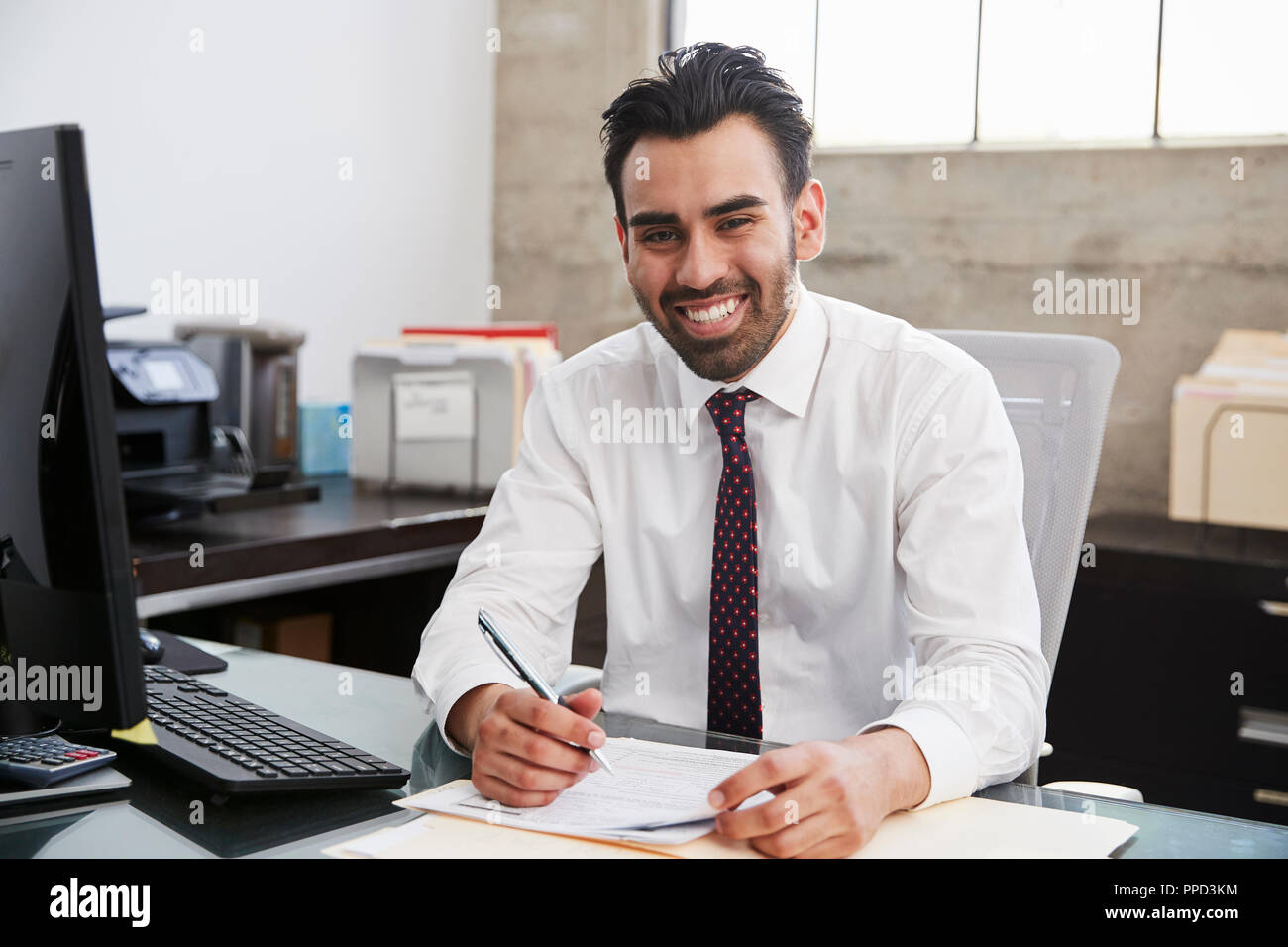 Young Hispanic male professional at desk smiling to camera Stock Photo