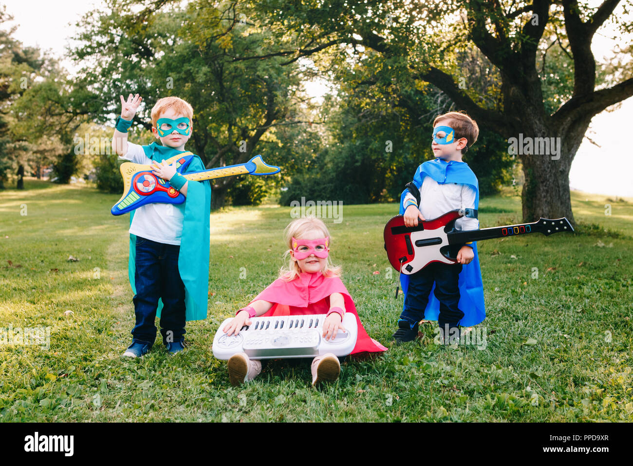 Cute adorable preschool Caucasian children playing superheroes music band rock group. Three kids friends having fun together outdoors in park. Happy a Stock Photo