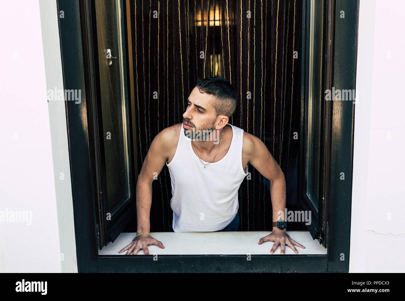 Young man with white shirt and half body outside the window looking curious to the outside Stock Photo