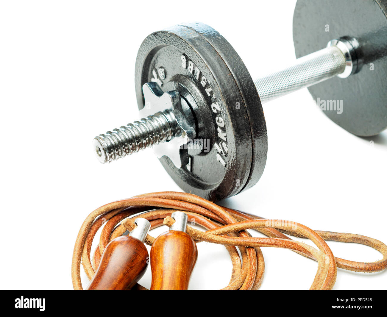 A single steel dumbbell and a leather skipping rope with wooden handles placed on a plain white background with no people Stock Photo
