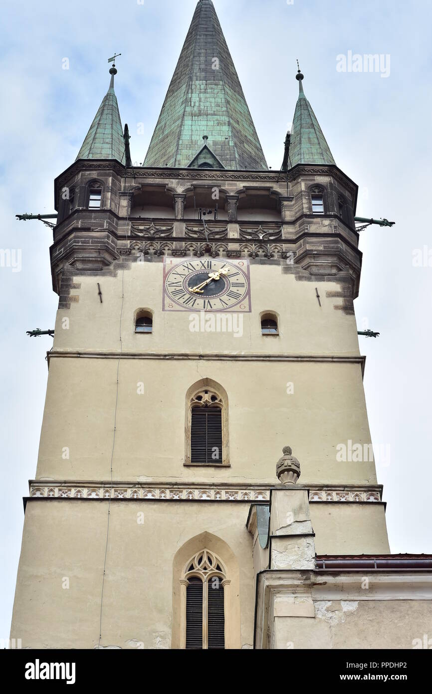 Belfry of gothic cathedral of Saint Nicholas in Presov with arched windows and porch under pointy roof. Clock on belfry wall uses Latin numerals. Stock Photo