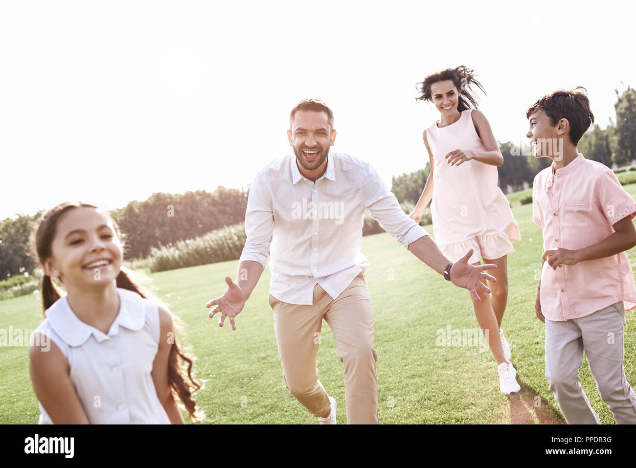 Bonding. Family of four running on grassy field playing playing  Stock Photo