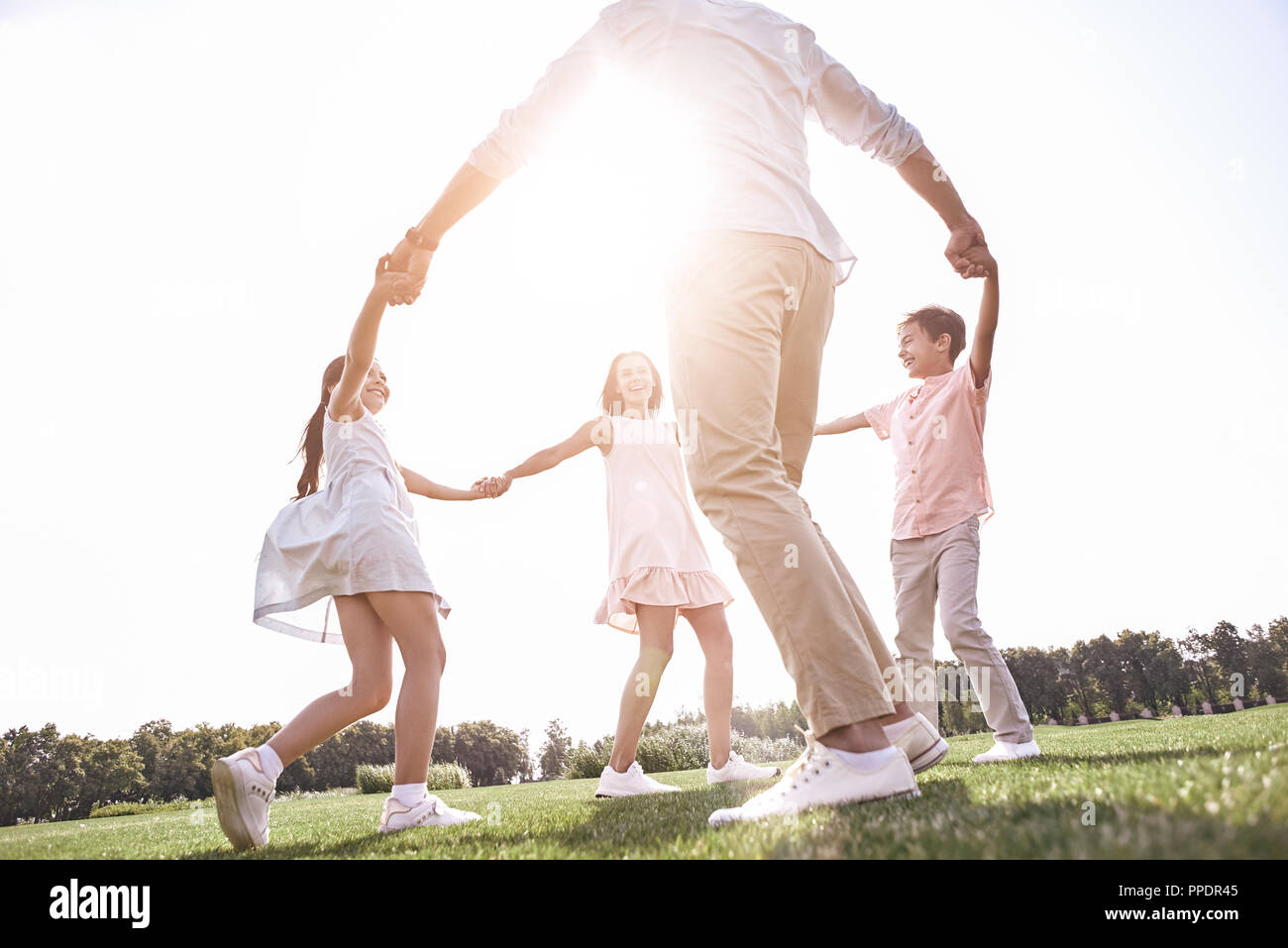 Bonding. Family of four holding hands dancing in circle on a gra Stock Photo