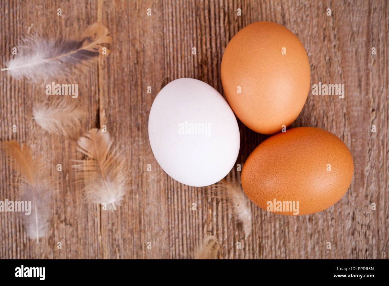 three eggs and feathers on rustic wooden table Stock Photo