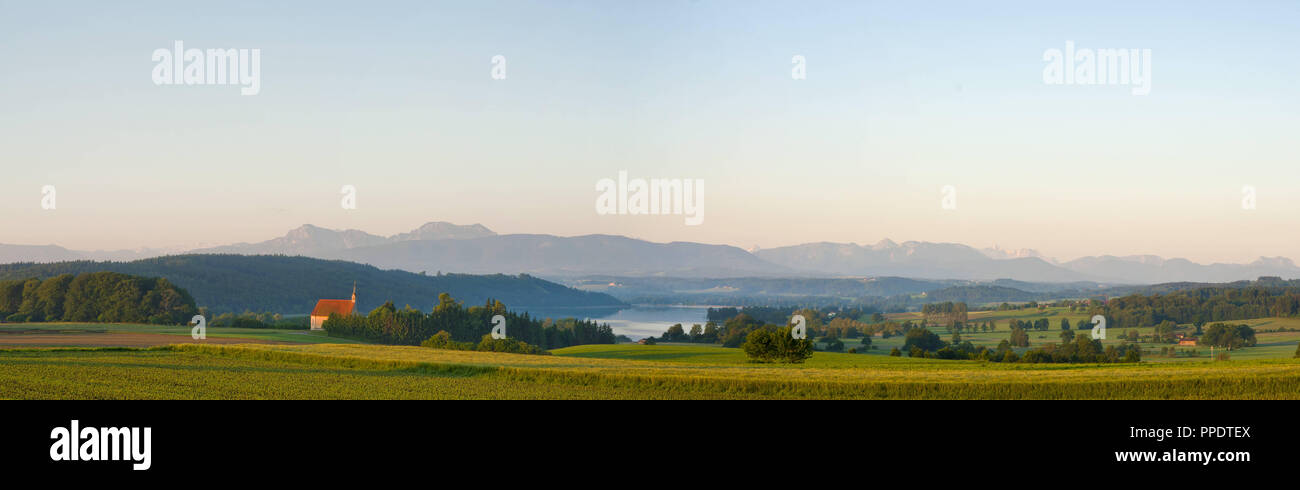 Panoramic landscape in early summer at Tachinger See (Lake Taching) with the St. Coloman Church in the foreground, in the background you can see the Maria Muehlberg with the Hochstaufen, Zwiesel and Teisenberg, Rupertiwinkel, the district of Traunstein in Upper Bavaria, Germany. Stock Photo
