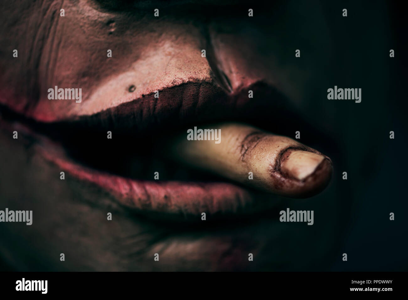 closeup of a scary disfigured man with a bloody amputated finger emerging from his mouth Stock Photo