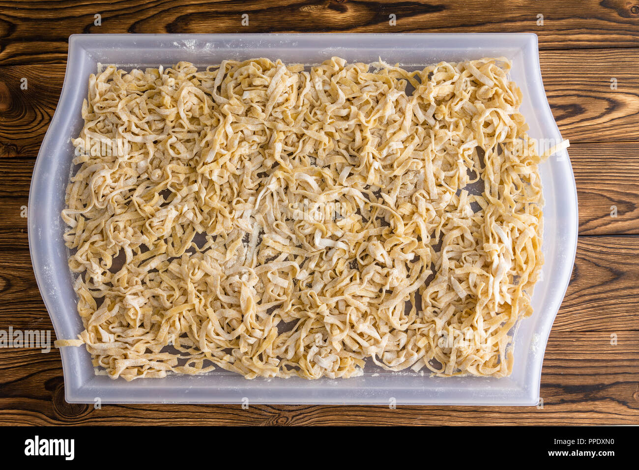 White tray of drying fresh homemade fettuccine pasta on a rustic wooden table viewed from overhead in a flat lay still life Stock Photo