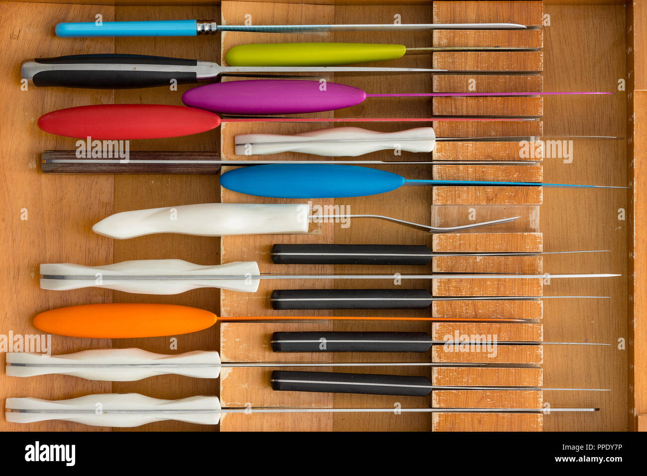 Neat arrangement of diverse knives in a fitted knife drawer in a wooden kitchen cabinet viewed from above in a close up full frame view Stock Photo