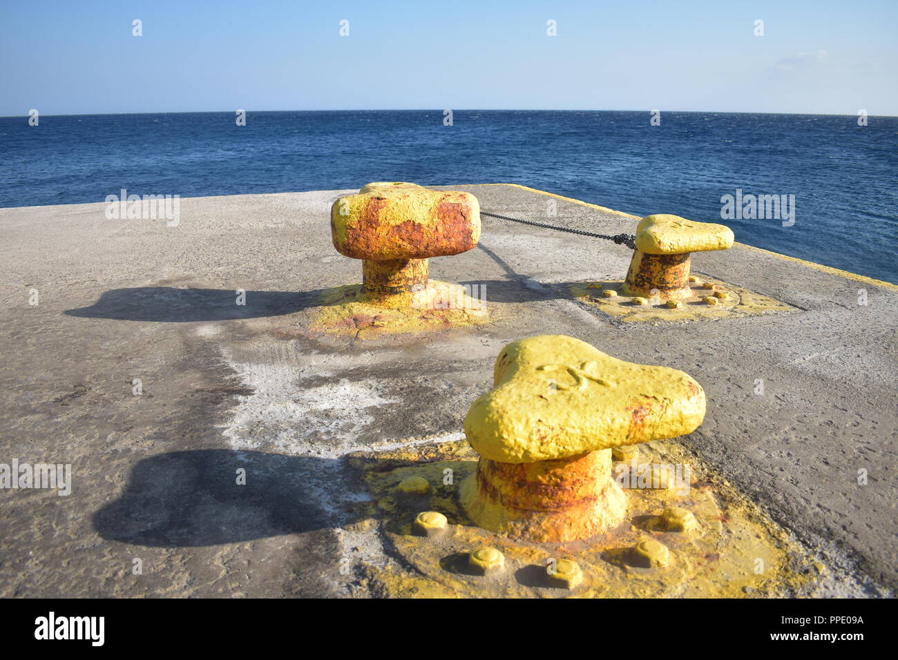 Greece, the charming, beautiful island of Sikinos.  Three yellow bollards for docking ferries, on the edge of the concrete jetty at the islands port.. Stock Photo