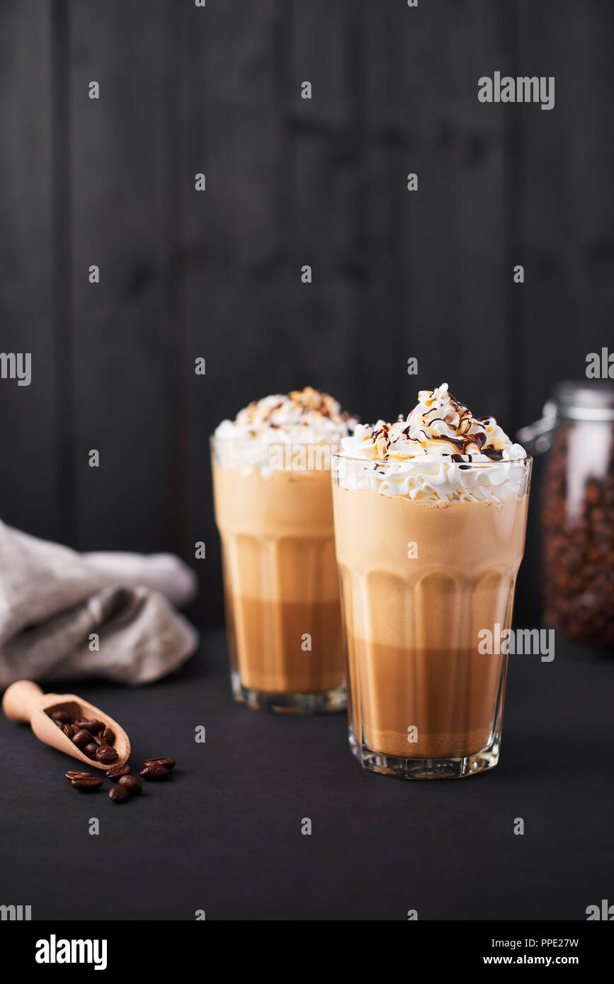 Iced caramel latte coffee in a tall glass with chocolate syrup and whipped cream. Dark wooden background with copy space. Stock Photo