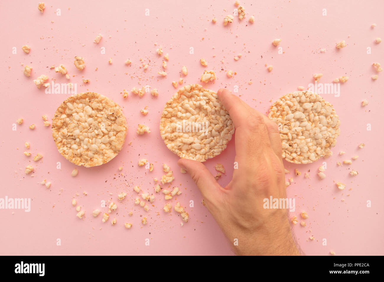 Rice cakes in male hand over pastel pink background, overhead view Stock Photo