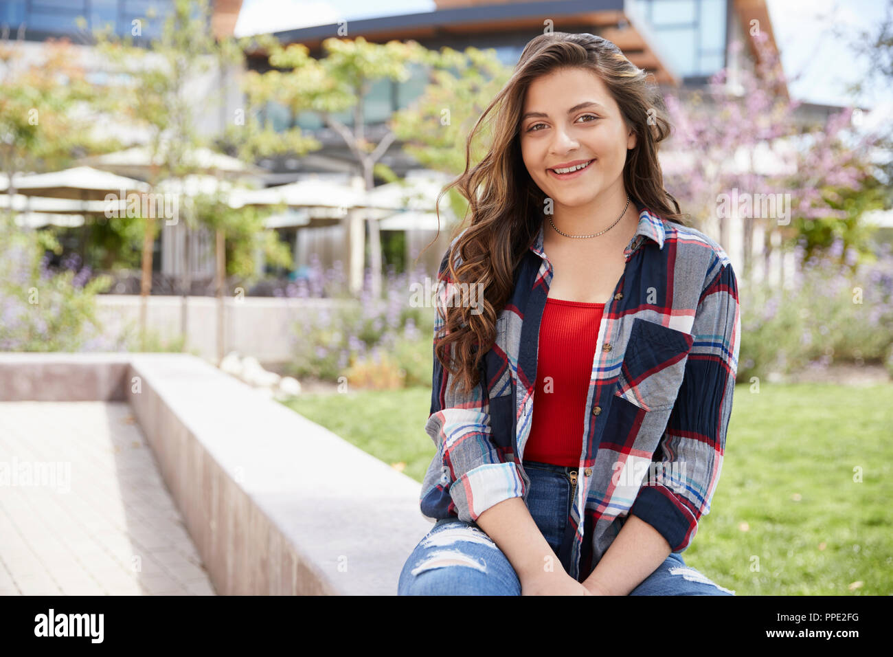 Portrait Of Female High School Student Sitting On Wall Outside College Buildings Stock Photo