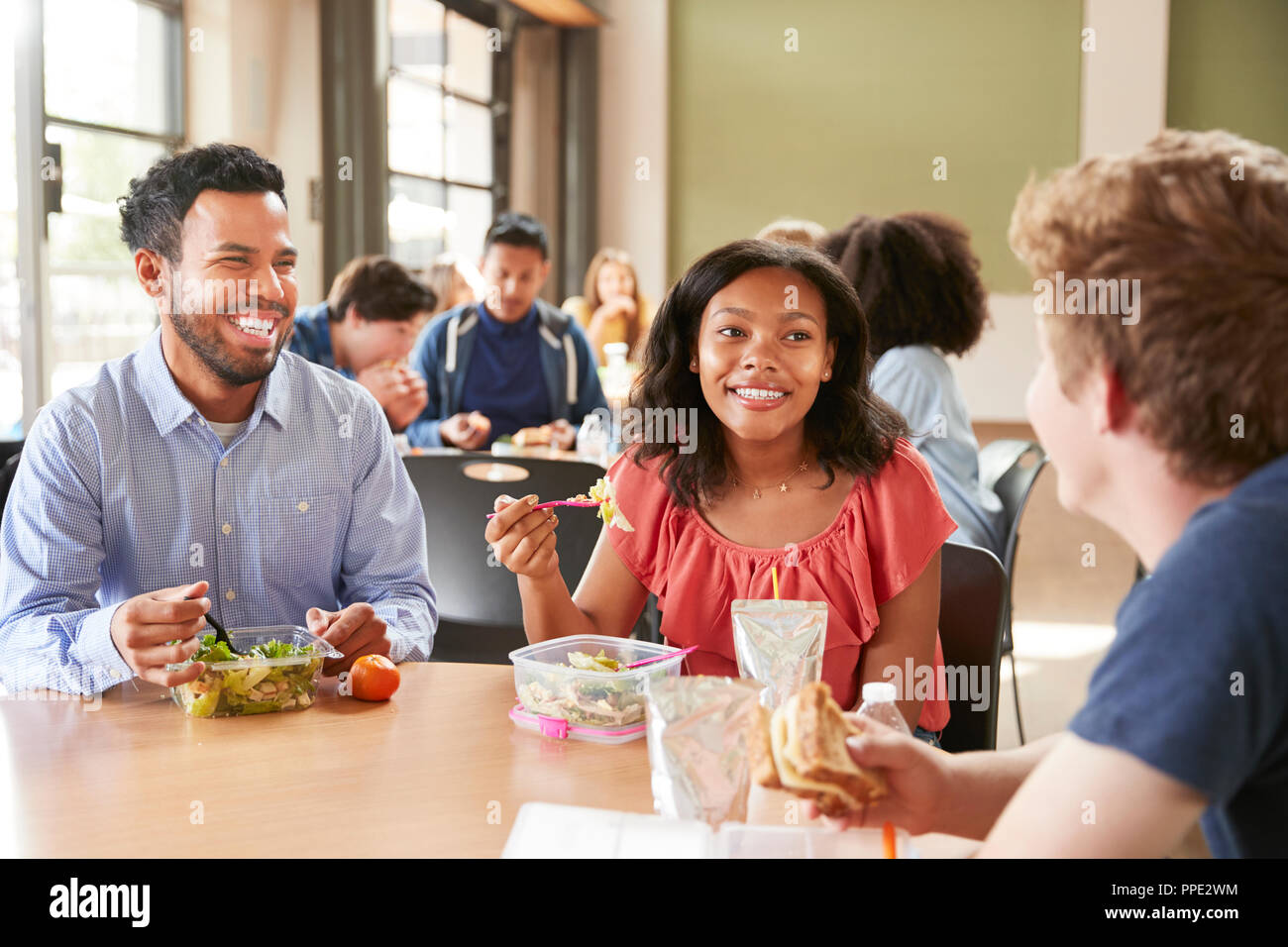 Teacher And Students Eating Lunch In High School Cafeteria During Recess Stock Photo