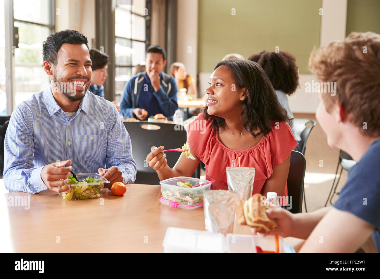 Teacher And Students Eating Lunch In High School Cafeteria During Recess Stock Photo