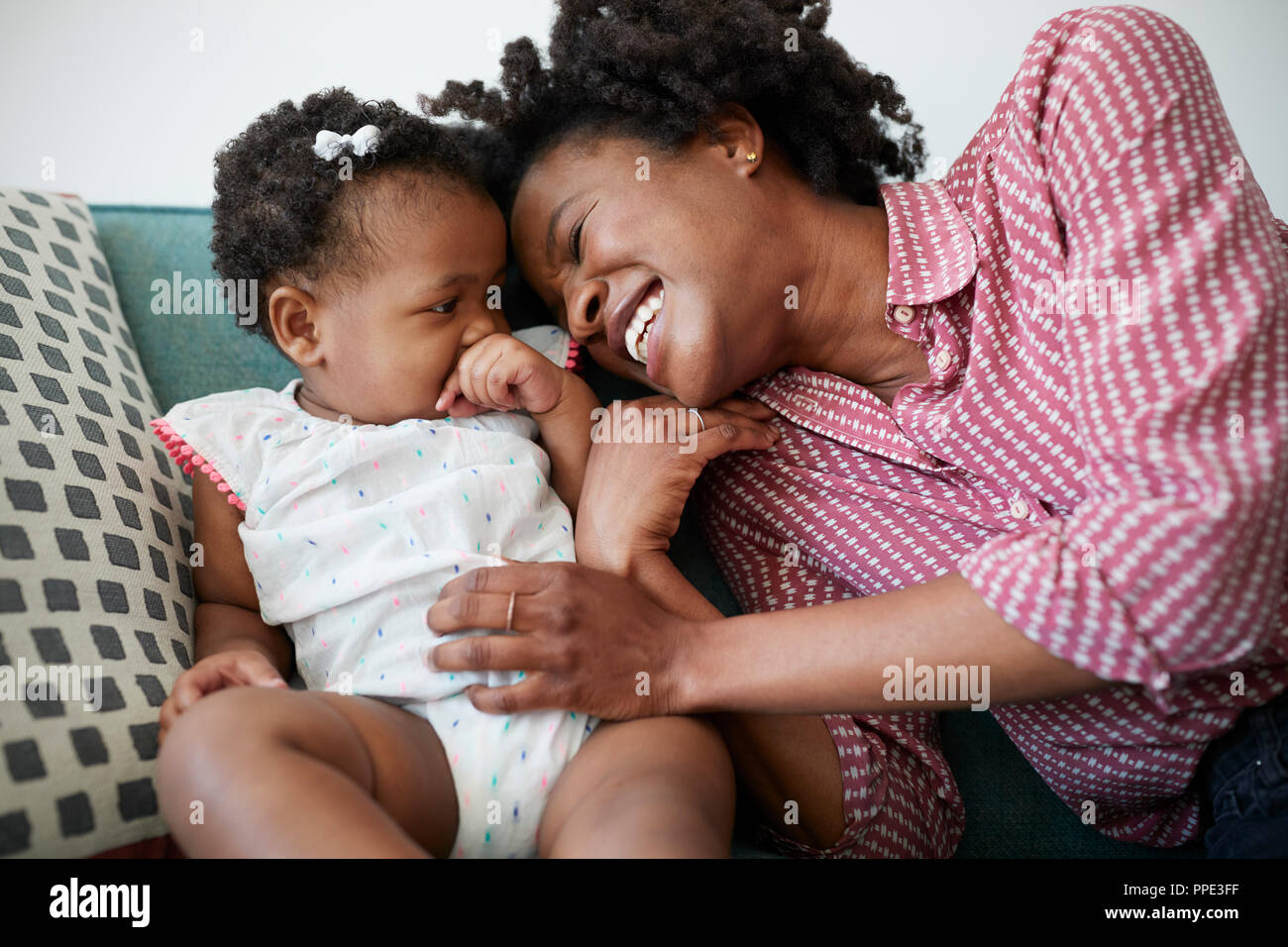 Mother Lying On Sofa At Home Playing With Baby Daughter Stock Photo