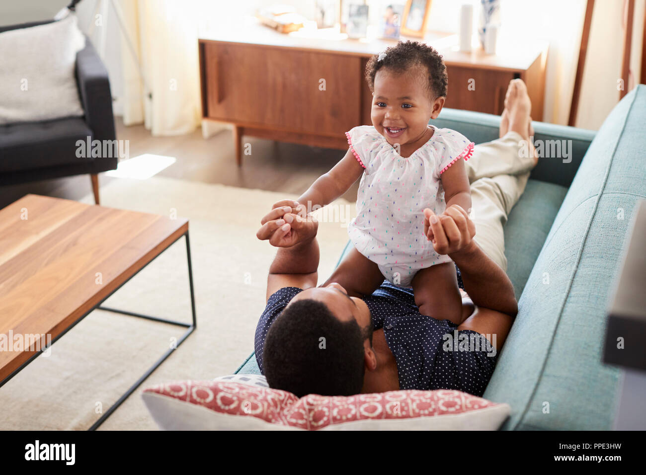 Father Lying On Sofa At Home Playing With Baby Daughter Stock Photo