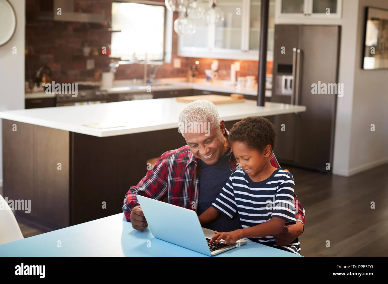 Grandfather And Grandson Sitting Around Table At Home Using Laptop Together Stock Photo