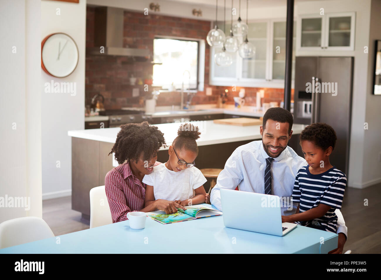 Parents Sitting Around Table At Home Helping Children With Homework ...