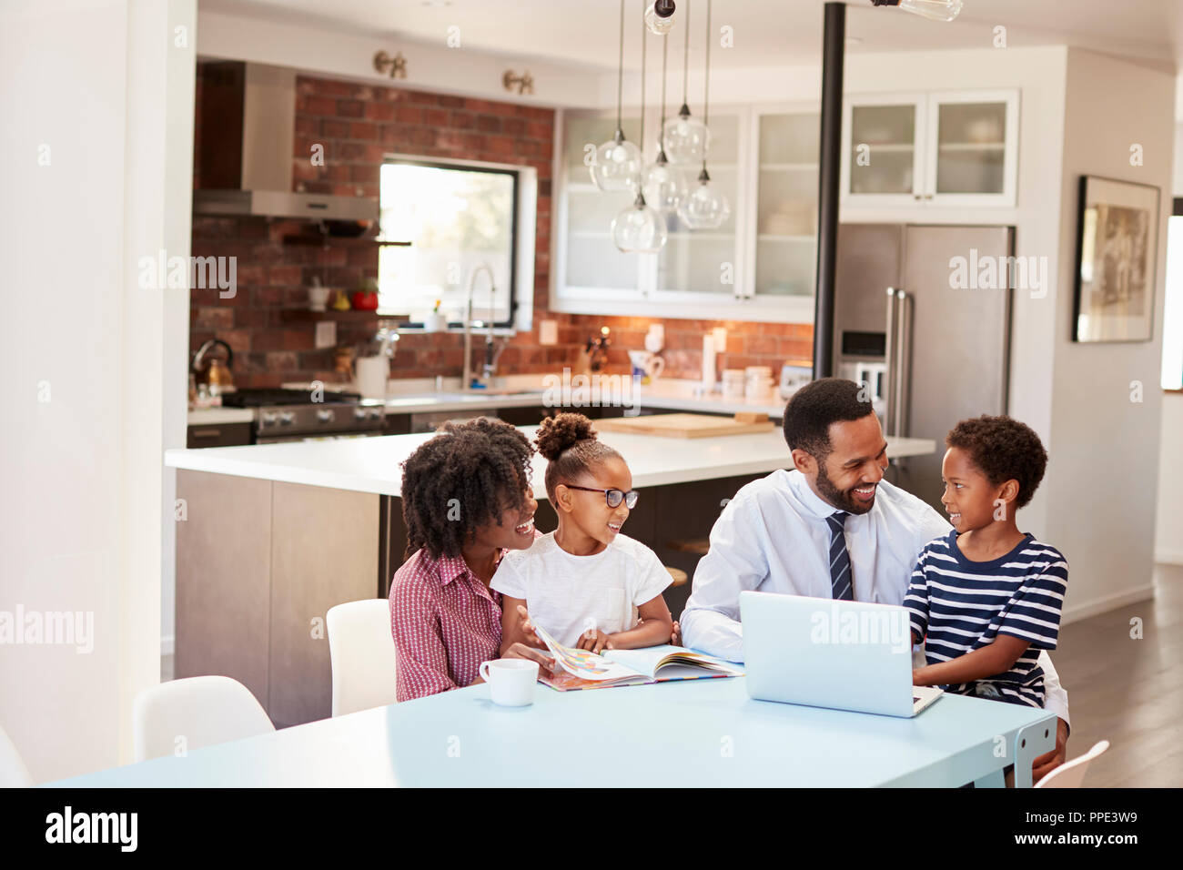 Parents Sitting Around Table At Home Helping Children With Homework ...