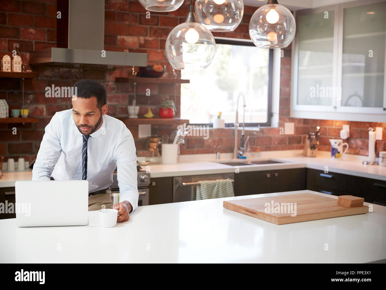 Businessman Using Laptop On Kitchen Island Before Leaving For Work Stock Photo