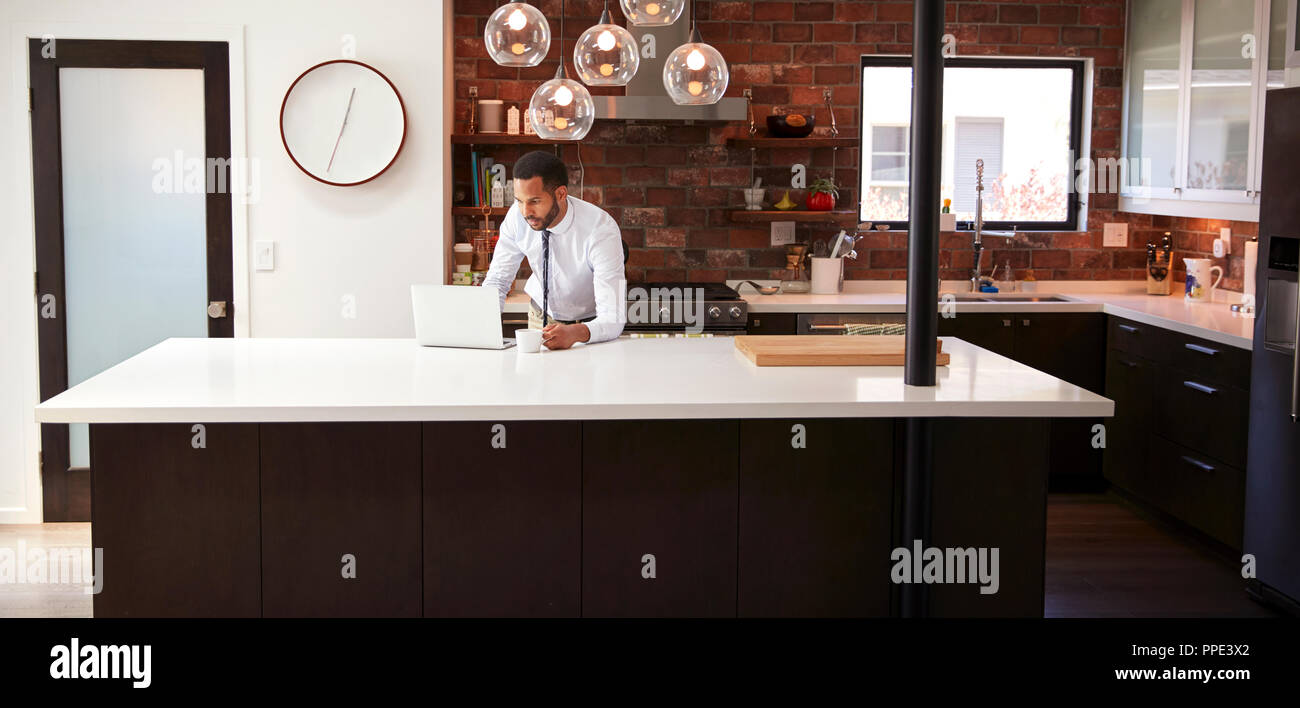 Businessman Using Laptop On Kitchen Island Before Leaving For Work Stock Photo